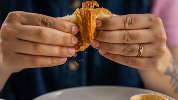 A person holding a pastry, with a plate of food and a small container on the table.