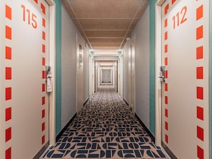 A hotel hallway with doors numbered 115 and 112, carpeted with a geometric pattern, and a ceiling with recessed lighting. - ibis budget Rennes Route de Saint Malo (Montgermont)