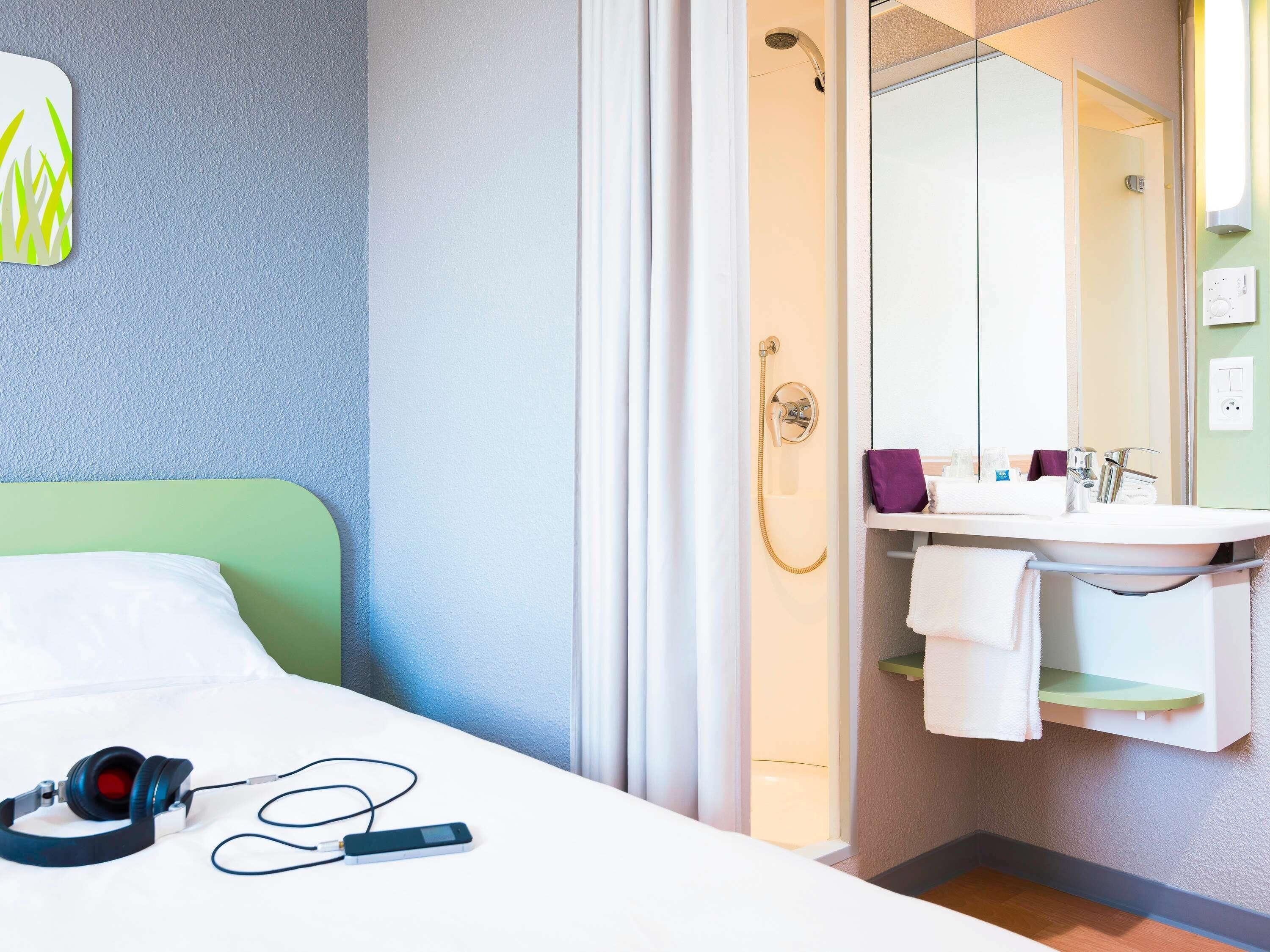 A hotel room with a bed, a shower, a sink, and a mirror.