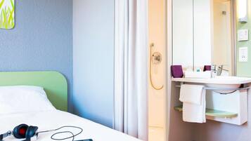 A hotel room with a bed, a shower, a sink, and a mirror.