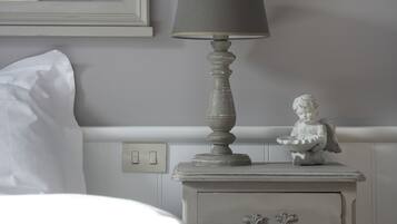 Una cama bien tendida con sábanas blancas, una mesita de noche con una lámpara y un pequeño objeto decorativo.
