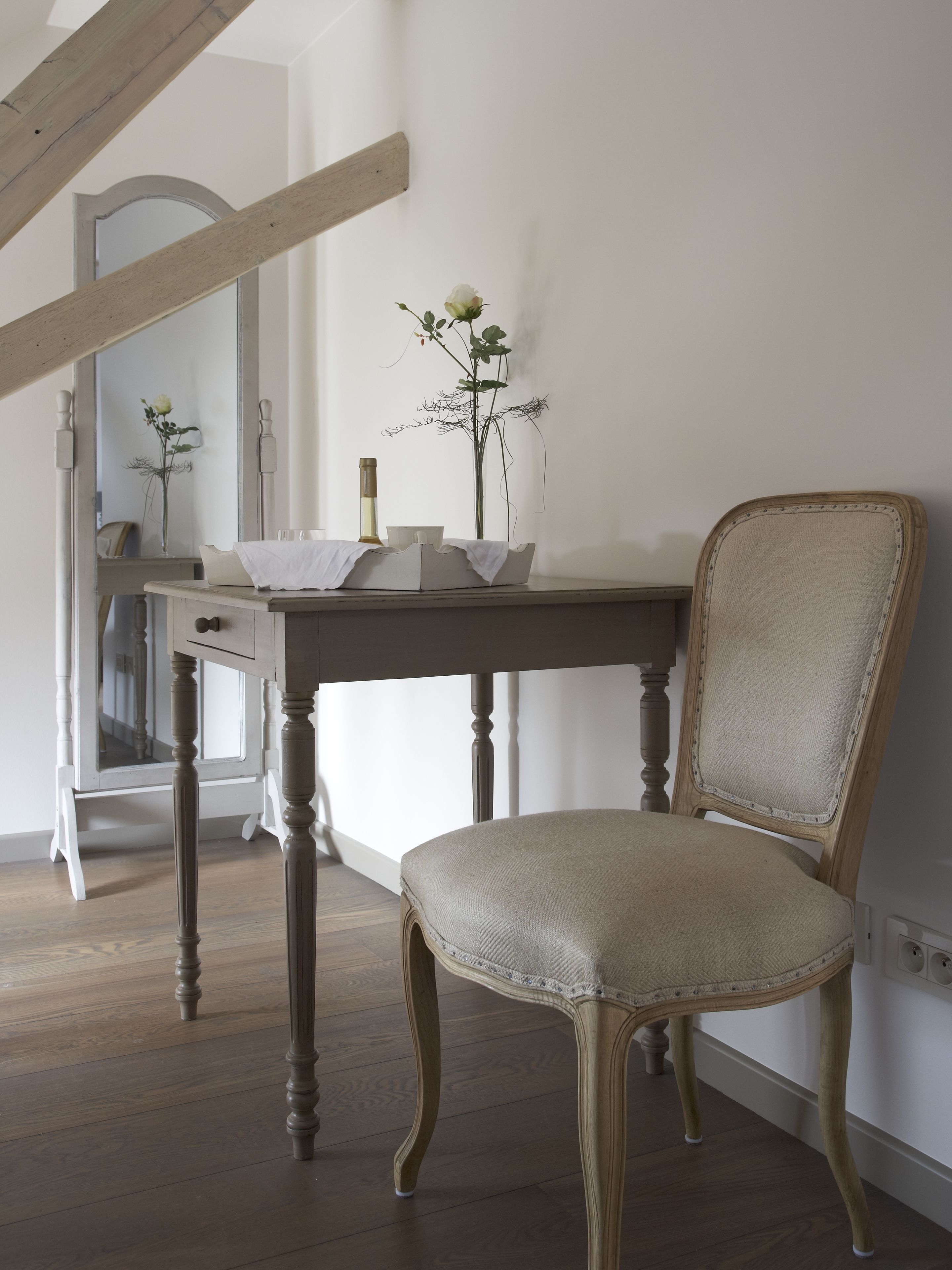 A room with a wooden dining table, a chair, a vase with flowers, and a mirror on the wall.