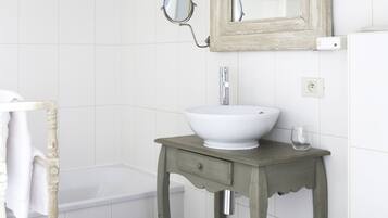 A bathroom with a white bathtub, a white sink with a mirror above it, and a wooden vanity with a drawer.