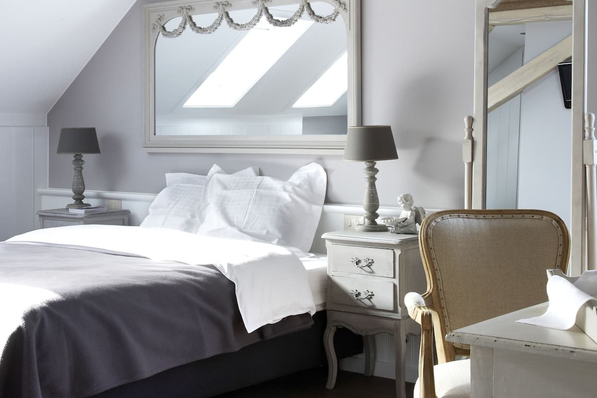 Une chambre à coucher comprenant un lit, des tables de chevet, une chaise, un miroir et une fenêtre de toit.