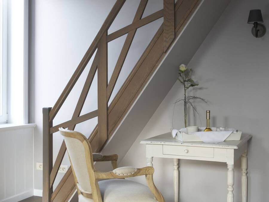Een kamer met een houten trap, een wit bureau met een vaas en een stoel.