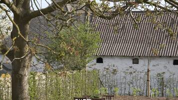 A traditional building with a tiled roof, surrounded by well-maintained hedges and a table with chairs set outdoors.