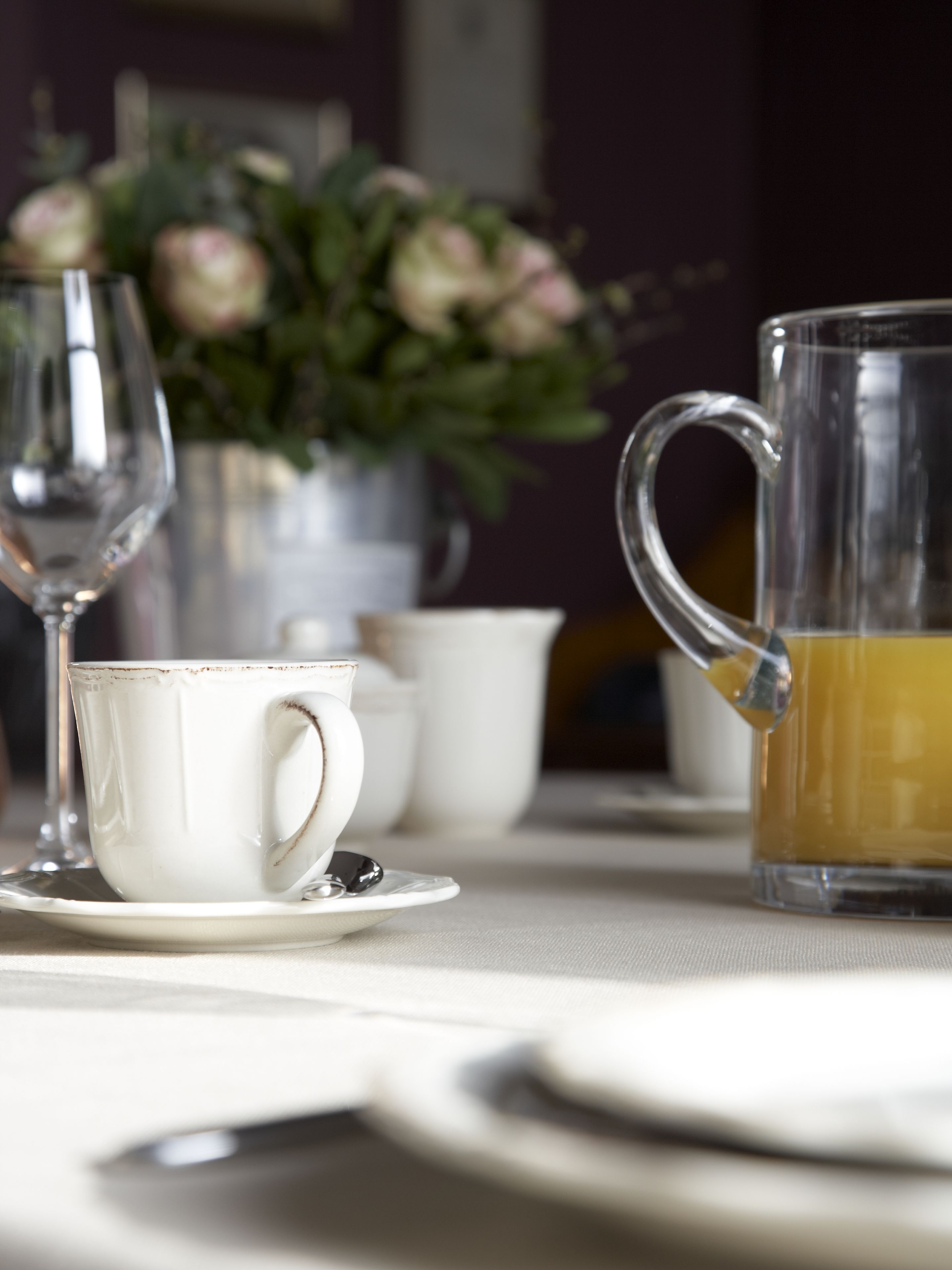 A table set with a white cup, saucer, and a clear glass pitcher.