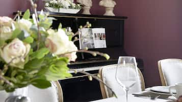 Una mesa de comedor con vajilla blanca, un jarrón con flores y un piano al fondo.