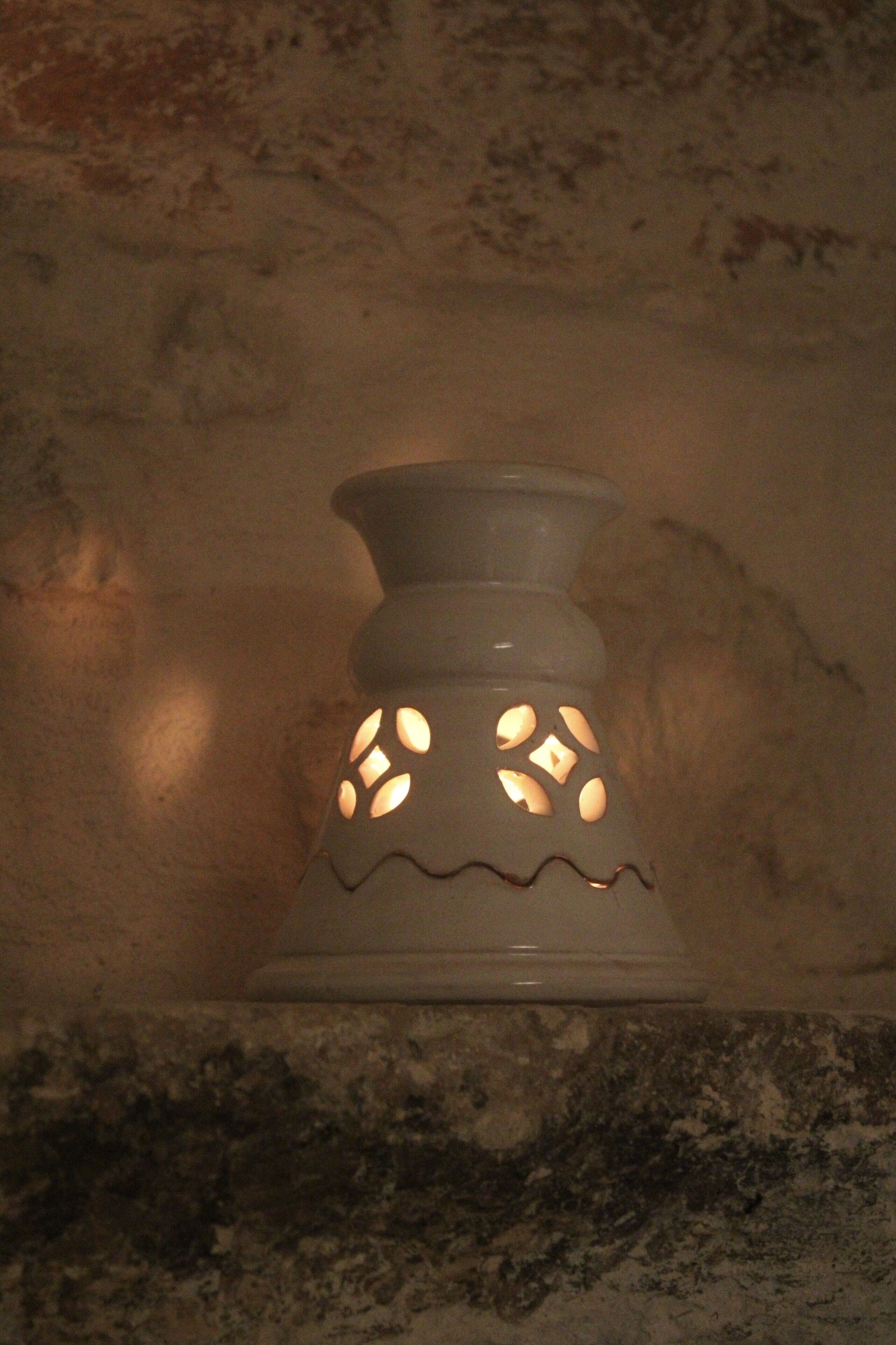 Un candelabro de cerámica blanca con diseños recortados sobre una pared con textura.