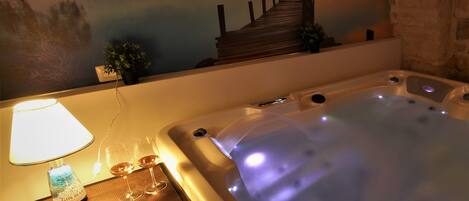 A spa area with a hot tub, a lamp, two glasses, and a candle on a table.