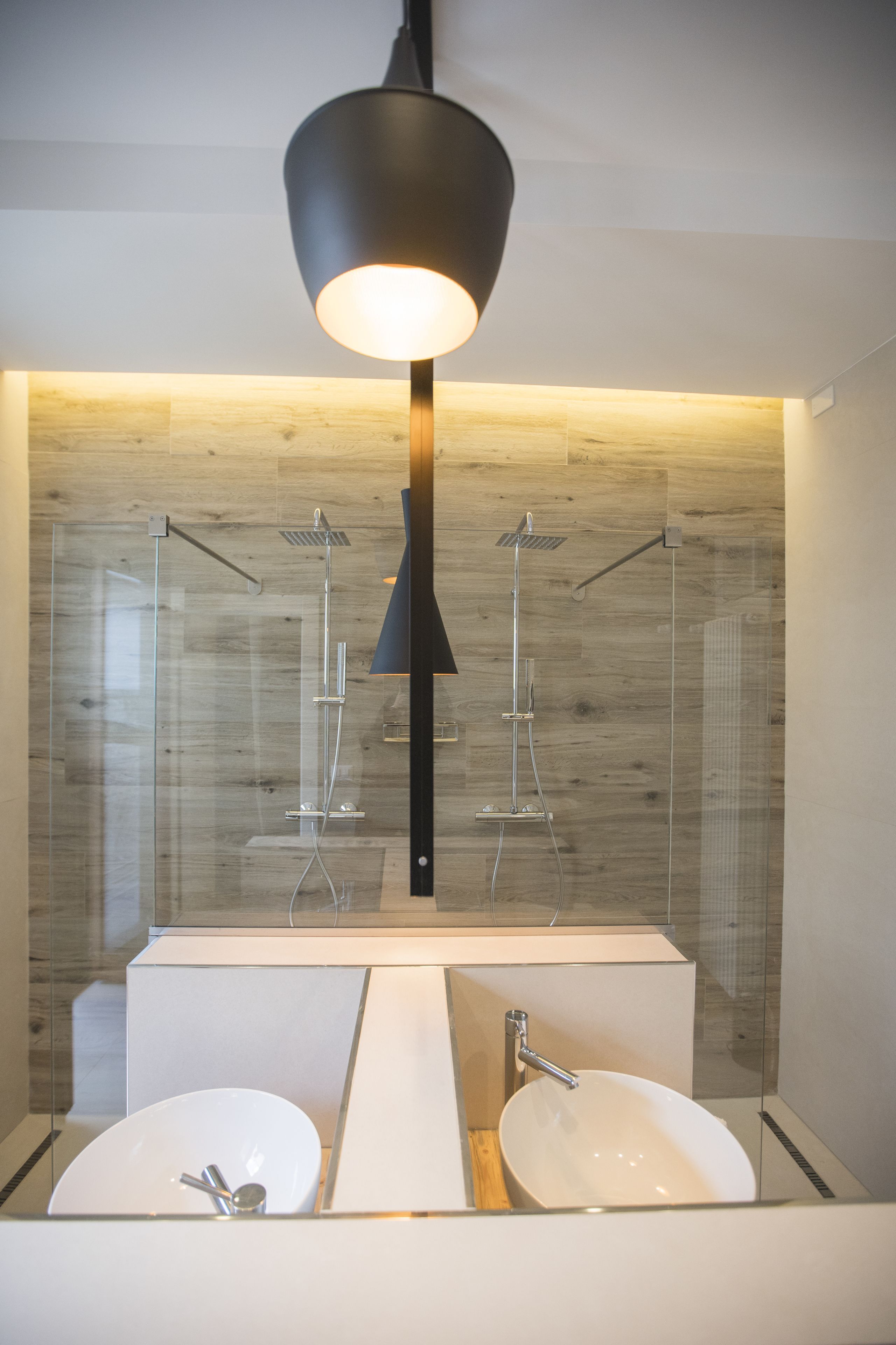 A modern bathroom with a large mirror, two sinks, a shower, and a pendant light.