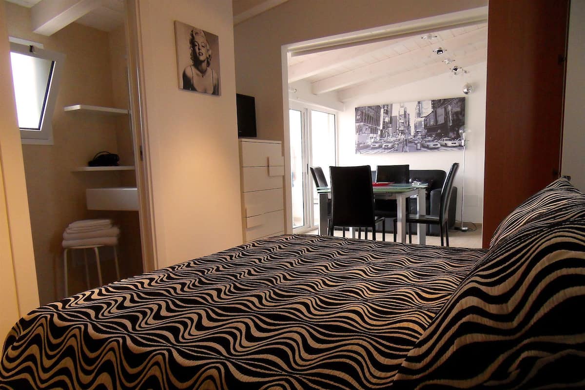 Quarto com cama, escrivaninha e cadeira, com vista para a rua.