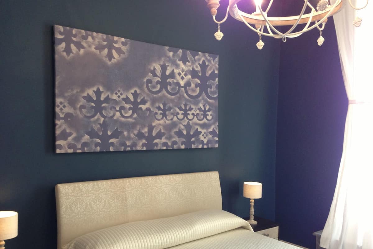 Quarto com cama, duas mesas de cabeceira, um candeeiro e uma obra de arte na parede.