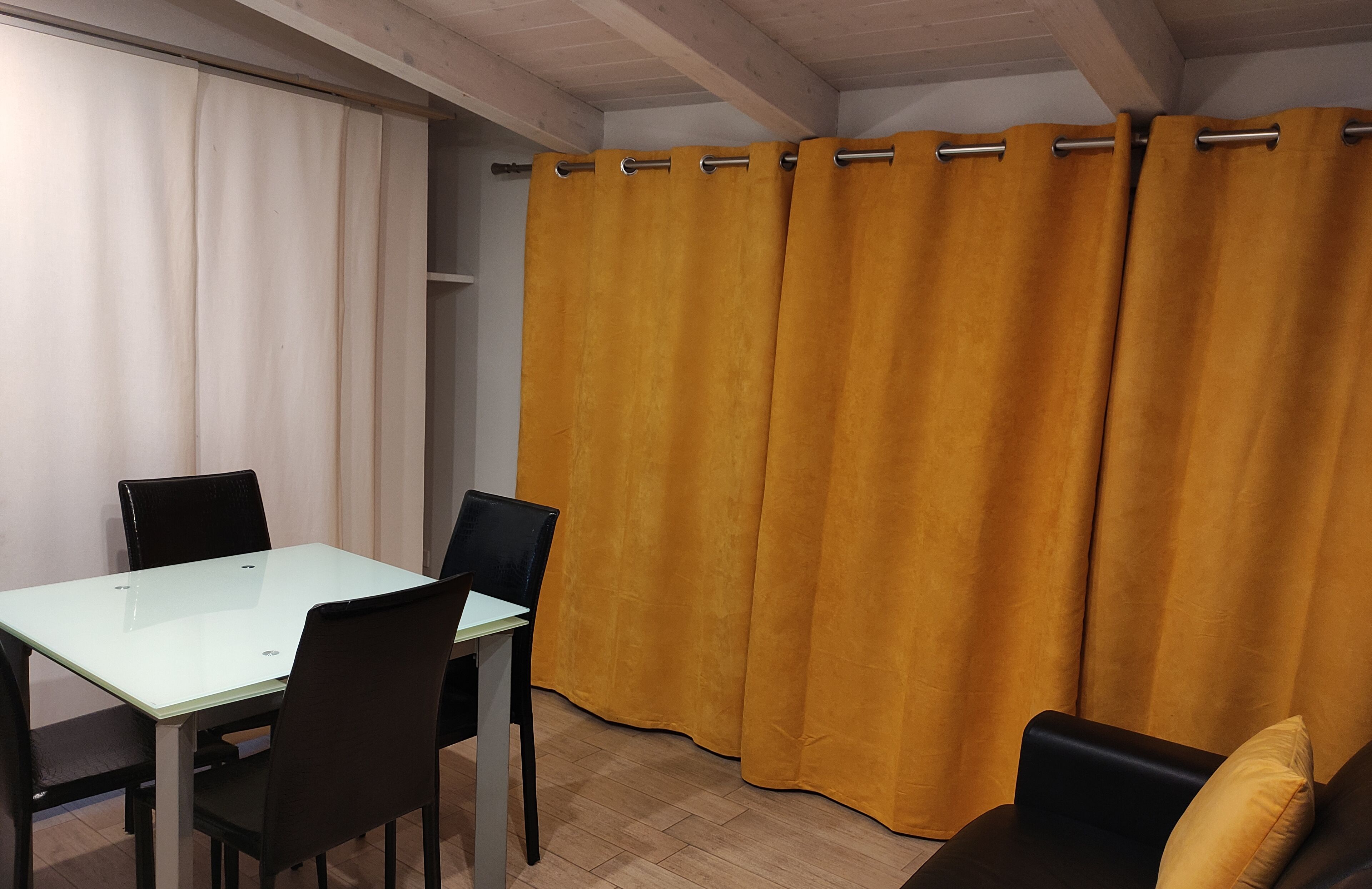 Una habitación con una mesa de vidrio, cuatro sillas, un sofá y una cortina amarilla.