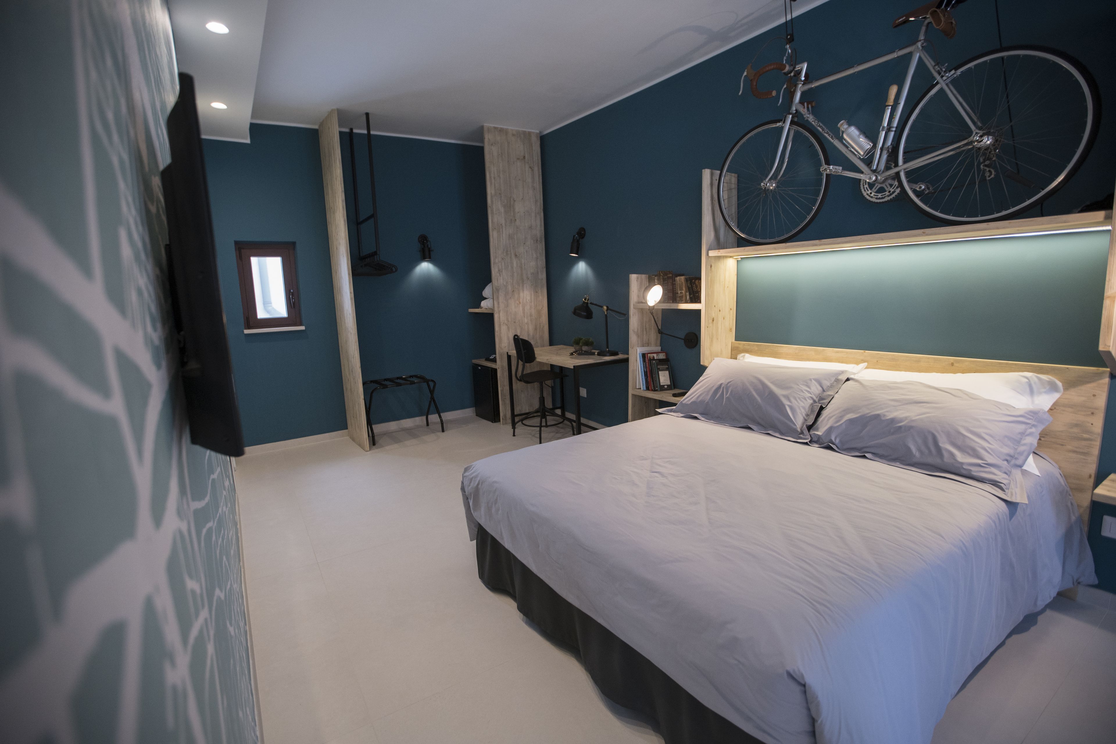 A bedroom with a bed, a desk, a chair, a bicycle, and a window.