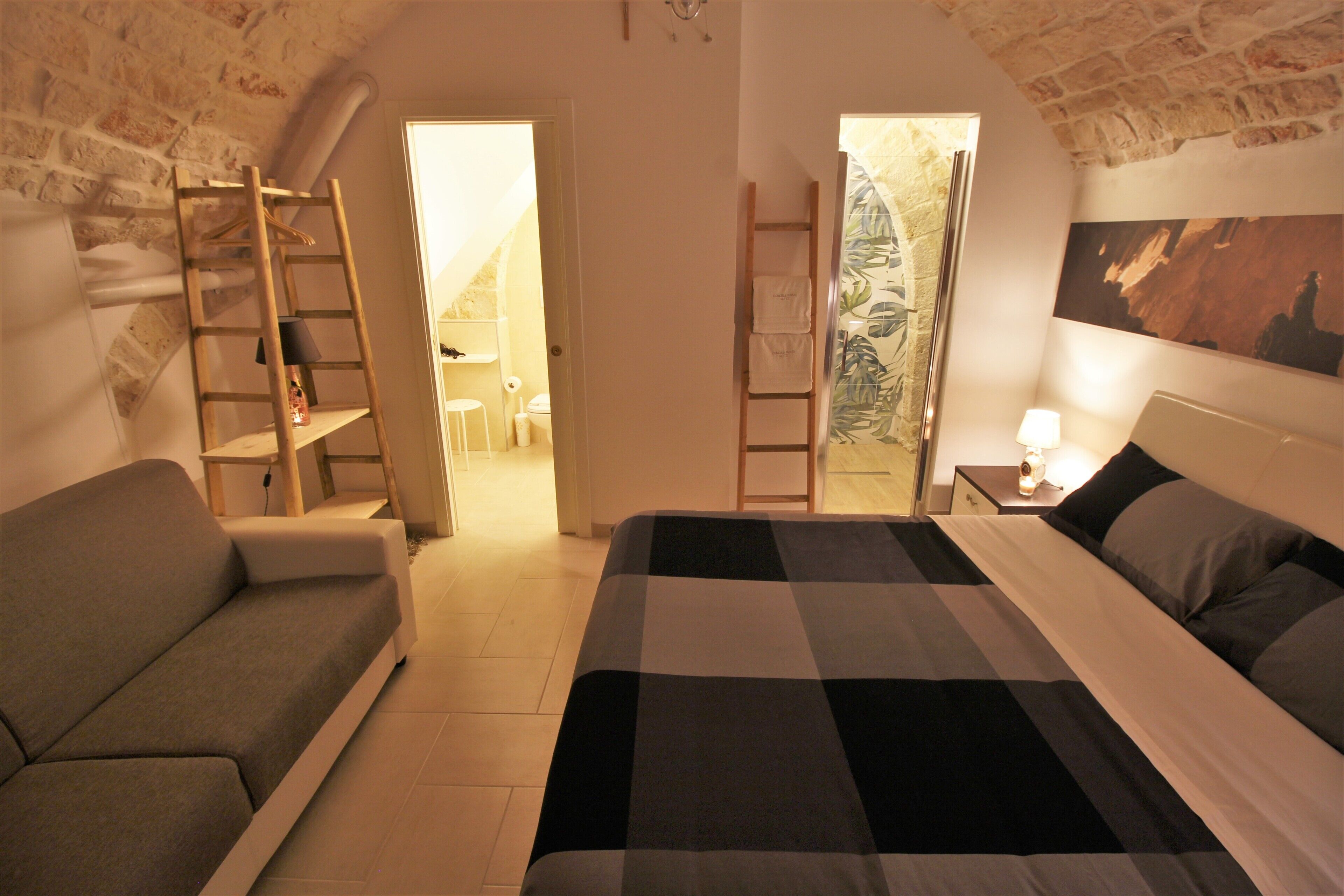 A bedroom with a bed, a sofa, a wooden ladder, and a painting on the wall.