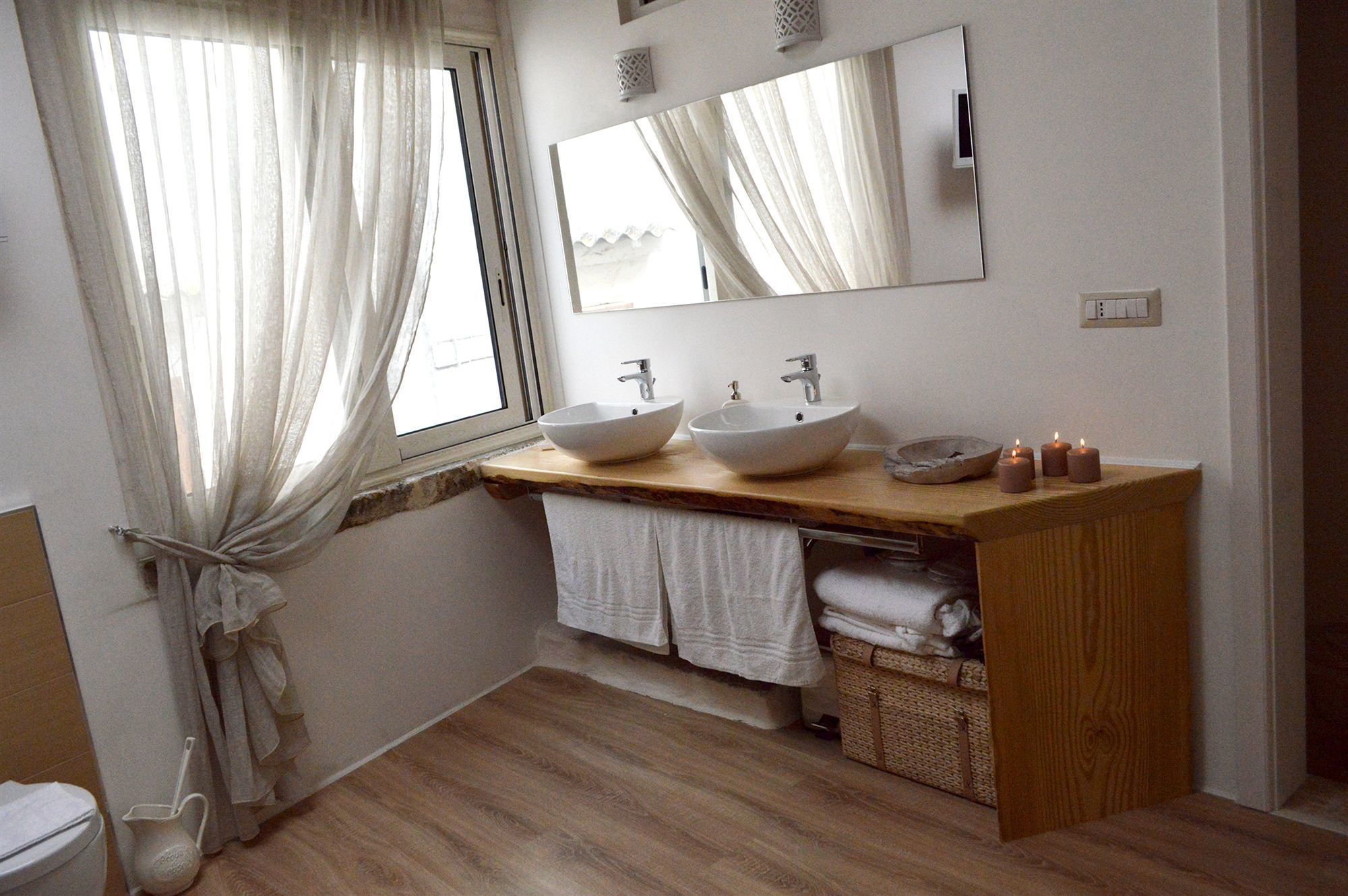 A bathroom with two sinks, a window with sheer curtains, a mirror, and a wooden vanity.