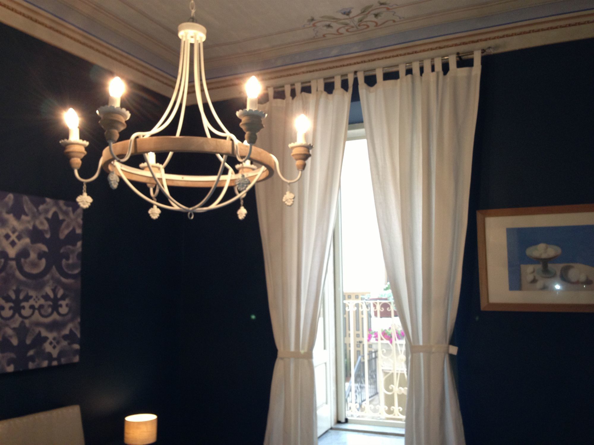 A chandelier with multiple light bulbs, white curtains, and a framed picture on the wall.