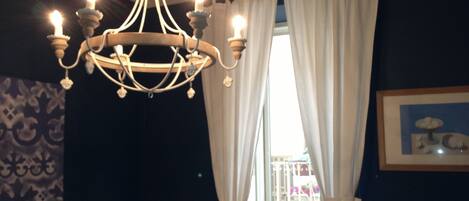 A chandelier with multiple light bulbs, white curtains, and a framed picture on the wall.