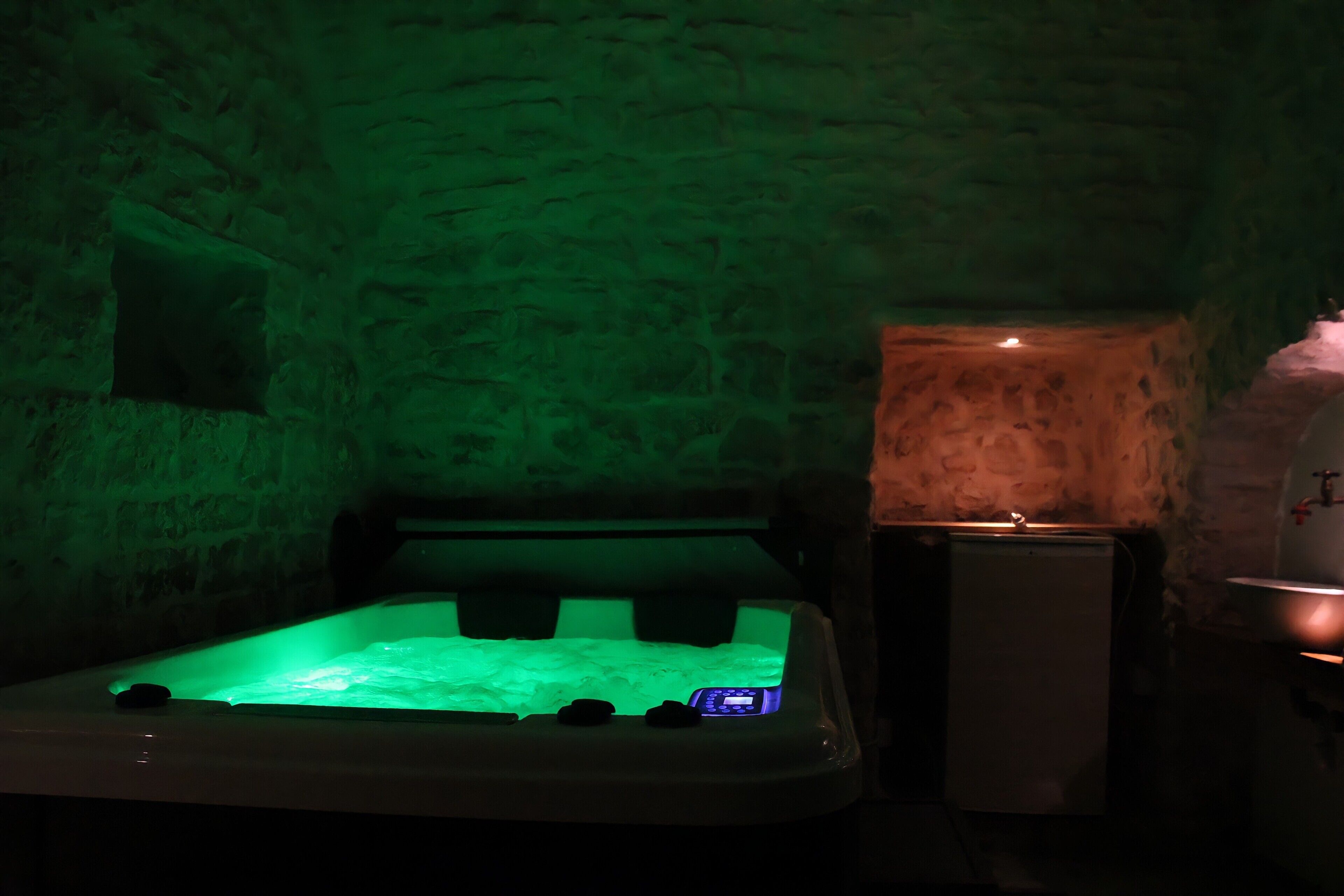 Ein Zimmer mit Steinwänden und einer Whirlwanne, beleuchtet mit grünem Licht.