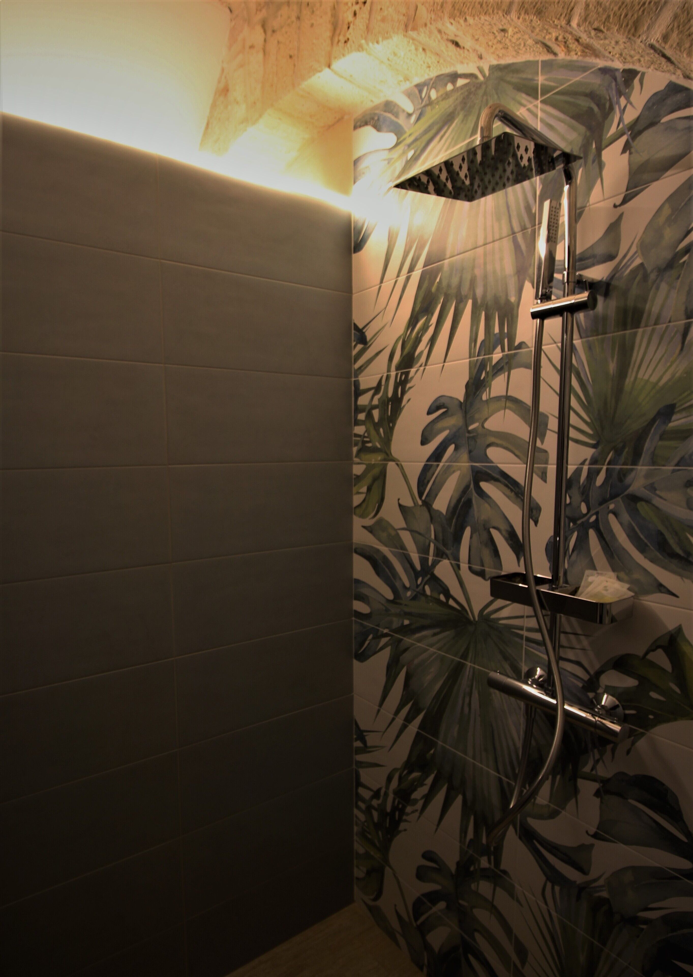 Een badkamer met een betegelde wand, een douche met behangpapier met een plantenmotief, en een houten plafond.