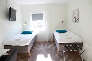 A hotel room with two single beds, a TV mounted on the wall, a window with curtains, a small table, and a chair. - Flygplatshotellet (Harryda)