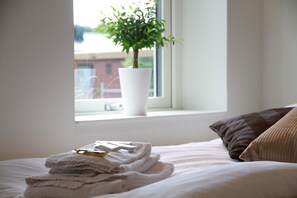 A neatly made bed with folded towels and a small potted plant on a windowsill. - Flygplatshotellet (Harryda)