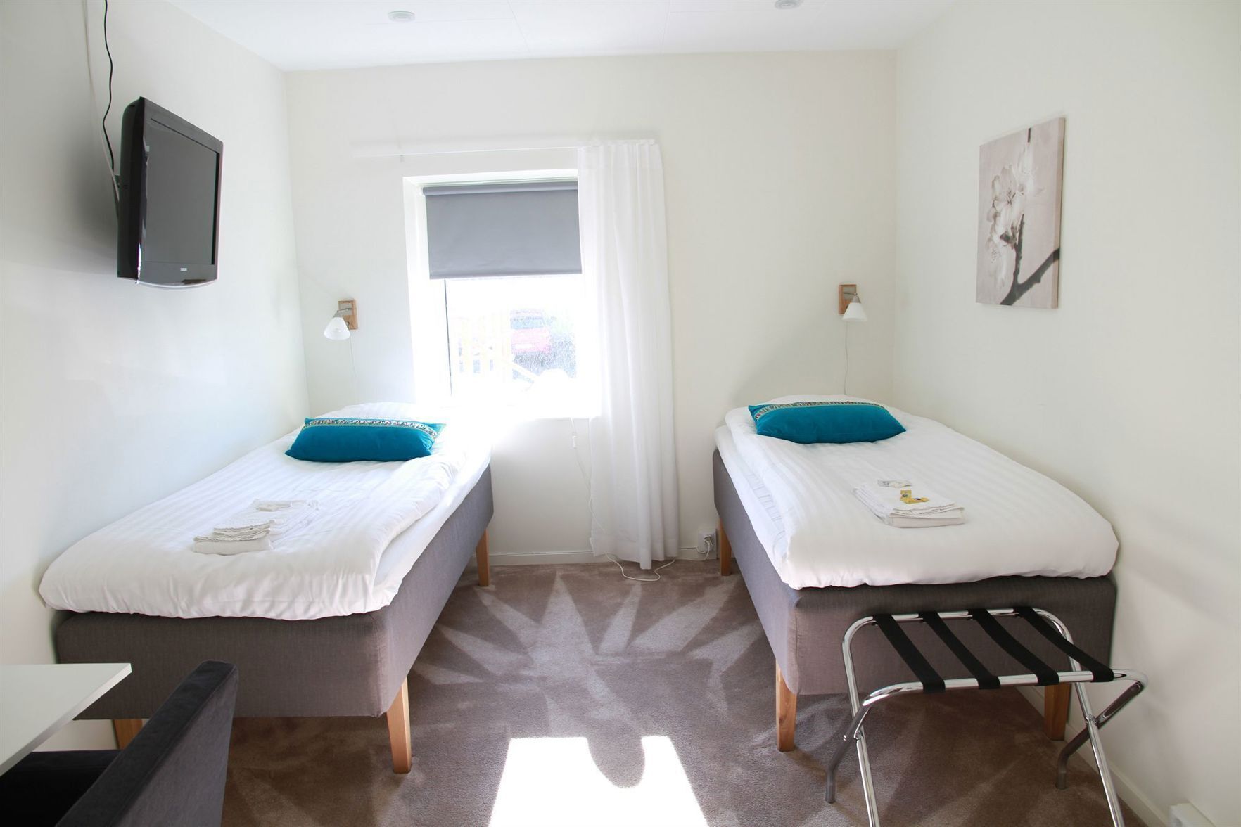 Una habitación con dos camas individuales, un escritorio, una silla, un televisor, una ventana con cortinas y un perchero.