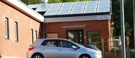 A hotel with a brick facade, a solar panel roof, and a car parked in front.