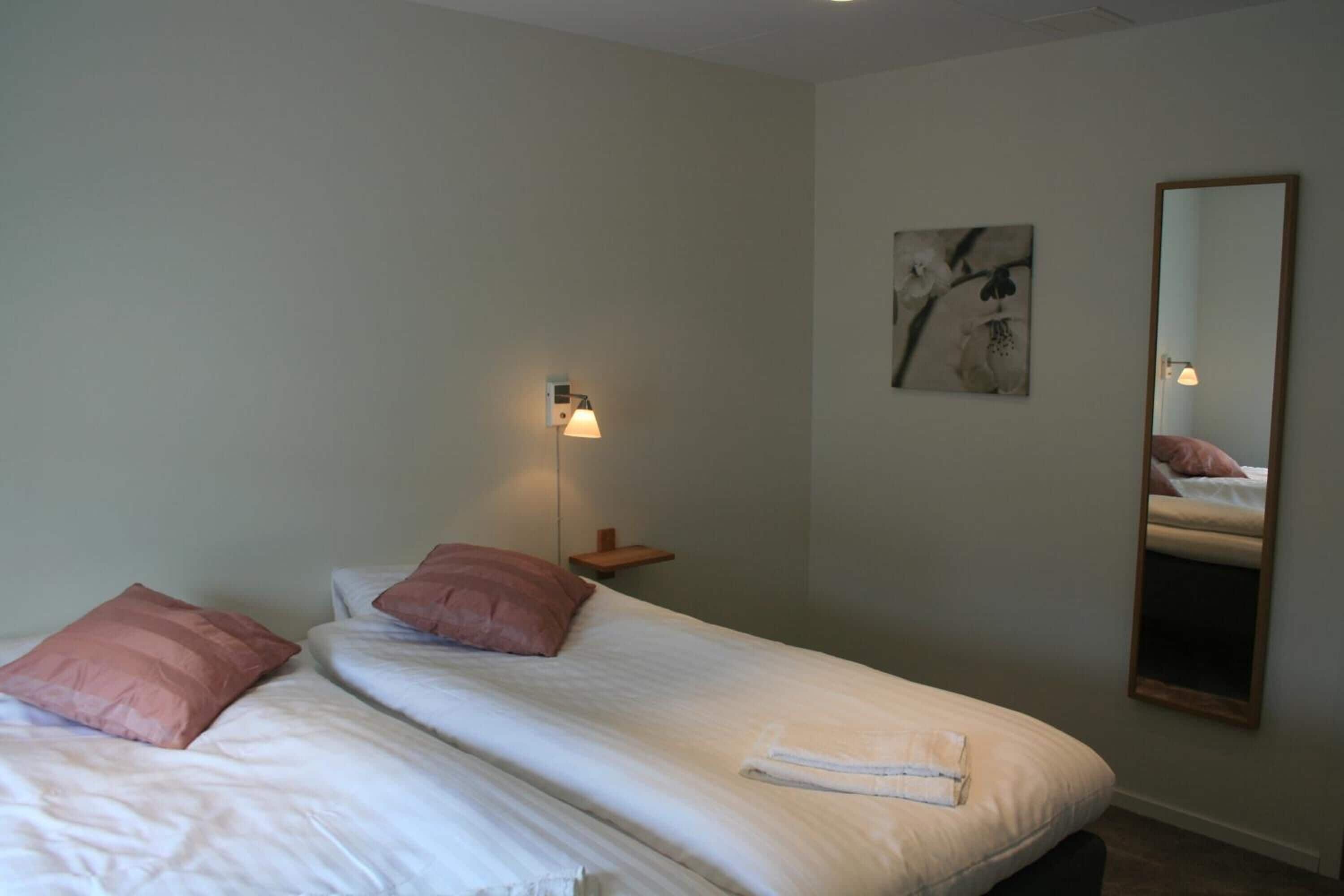 Un dormitorio con dos camas, una mesita de noche, una lámpara, un espejo y una obra de arte en la pared.
