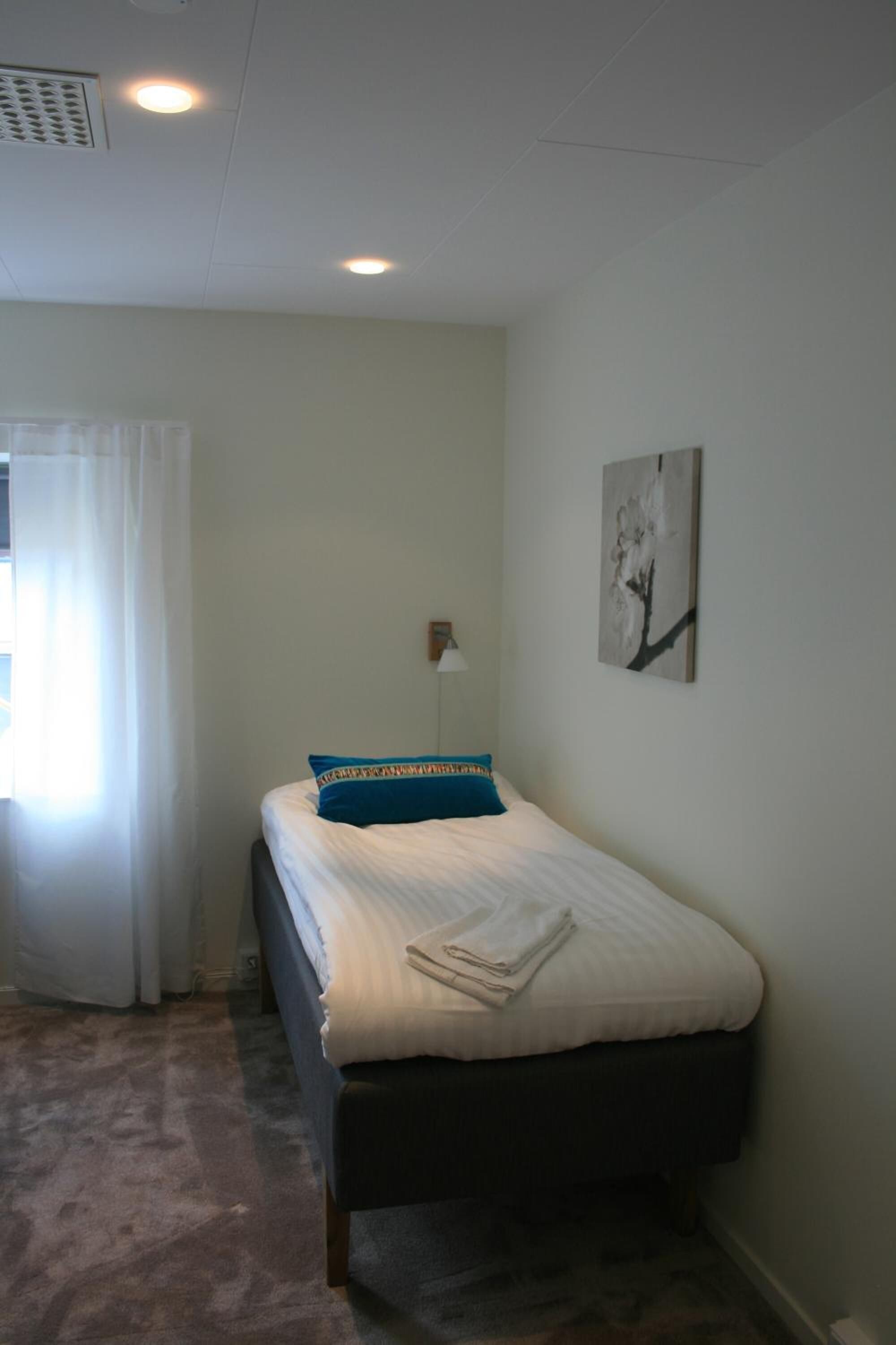 Un dormitorio con cama, una mesita de noche, una lámpara y un cuadro en la pared.