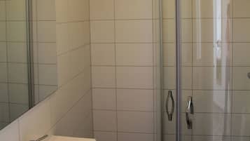 Een moderne badkamer met een douchecabine van glas, een wastafel met spiegel en een handdoek aan de douchedeur.