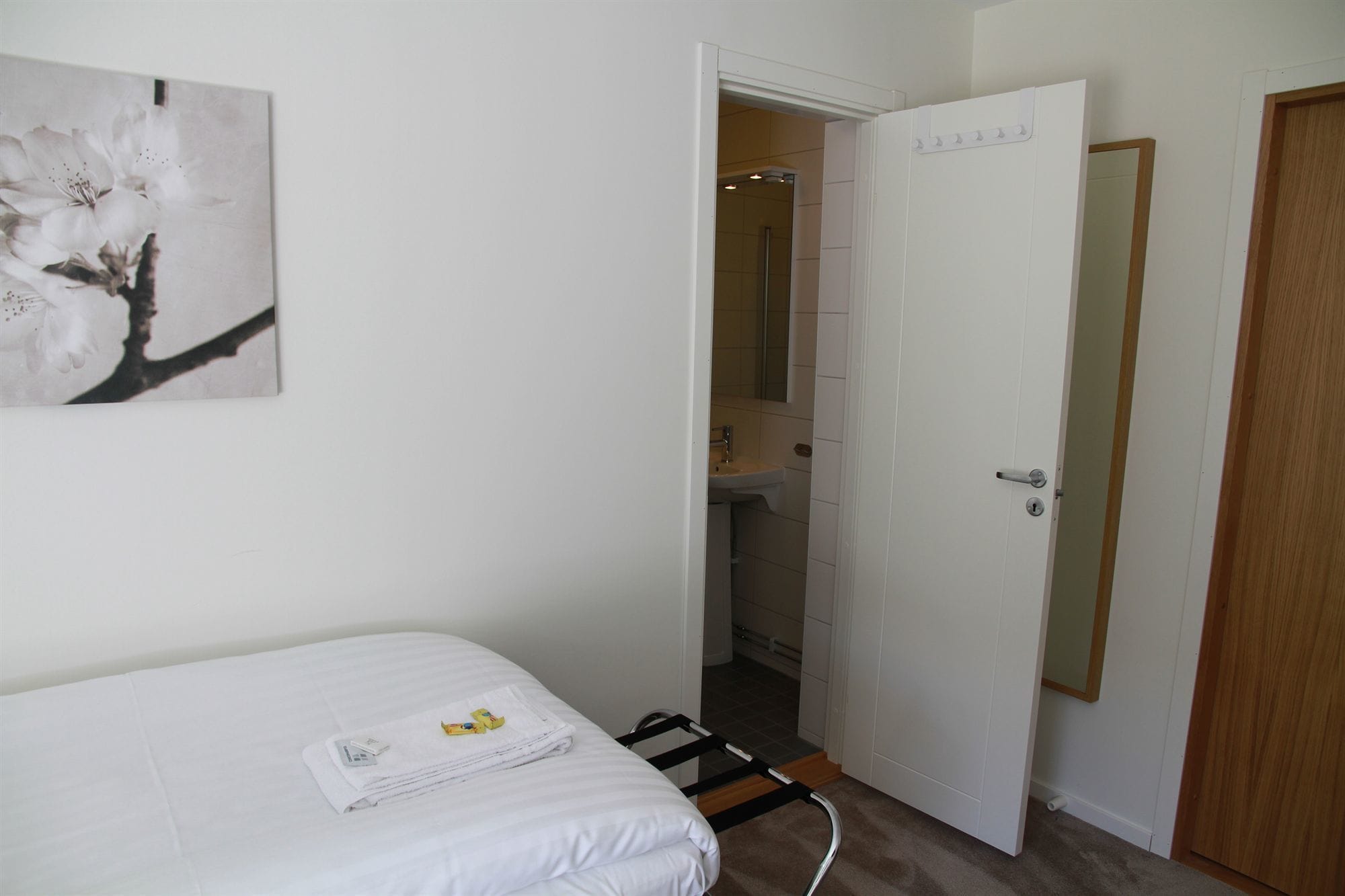 A hotel room with a bed, a bathroom with a sink and mirror, and a door leading to another room.