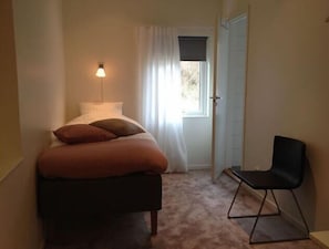 A bedroom with a bed, a chair, a lamp, and a window with curtains. - Flygplatshotellet (Harryda)