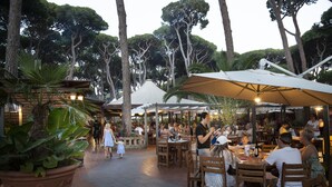 Een terras met houten tafels en stoelen, grote parasols en potplanten.