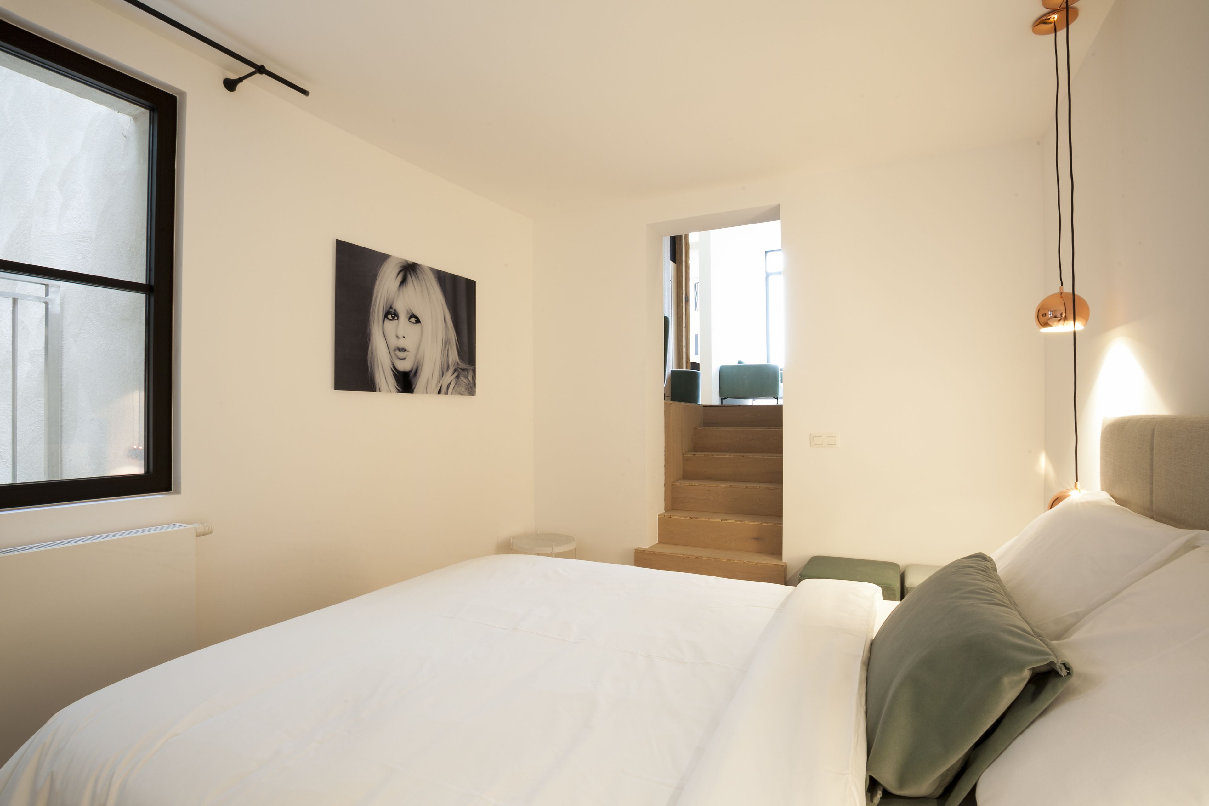 Een slaapkamer met een bed, een schilderij aan de muur, een trap en een hanglamp.