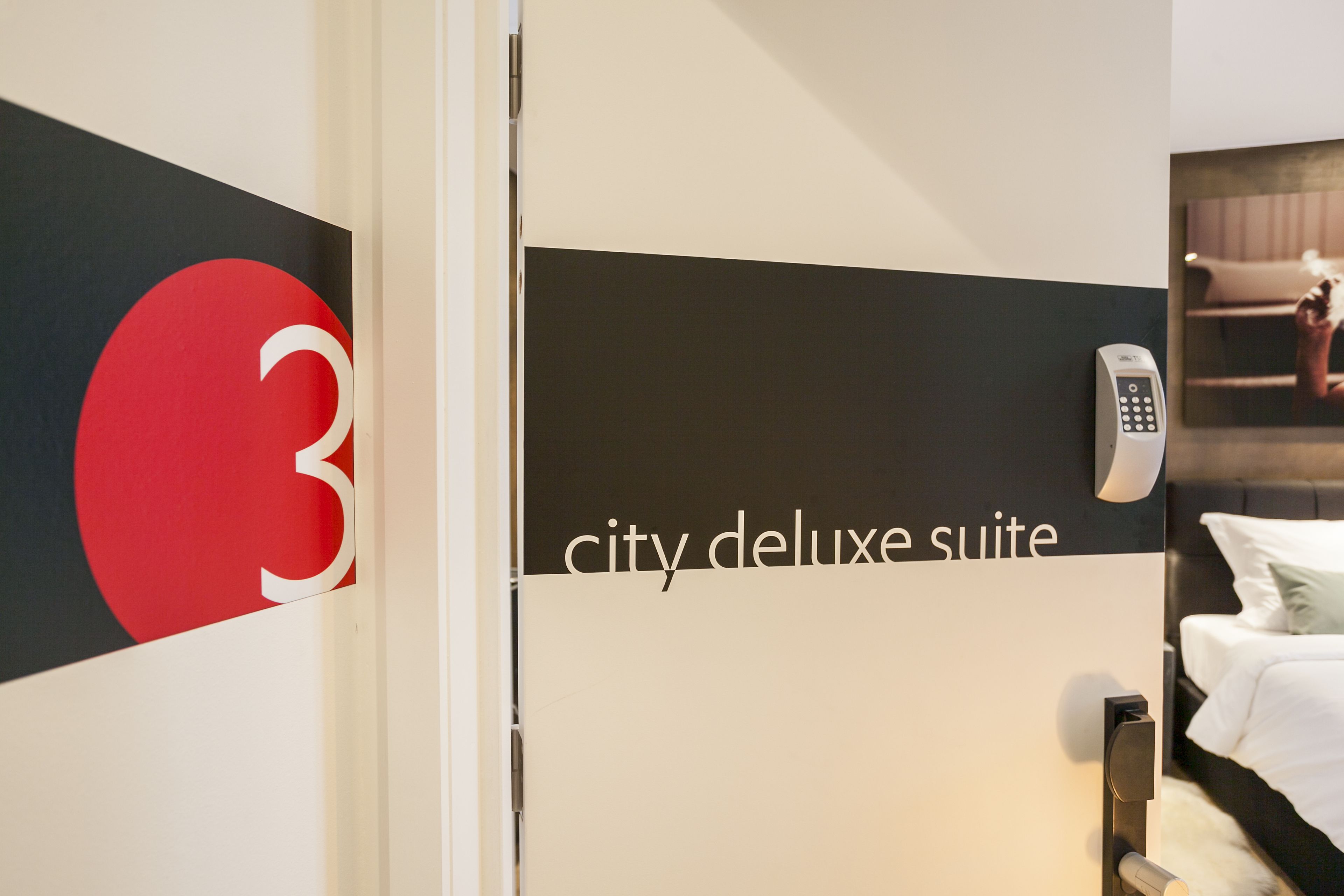 Een hotelkamer met een bed, een aan de muur bevestigd telefoontoestel en een bordje dat aangeeft dat de kamer deel uitmaakt van de 'city deluxe suite'.