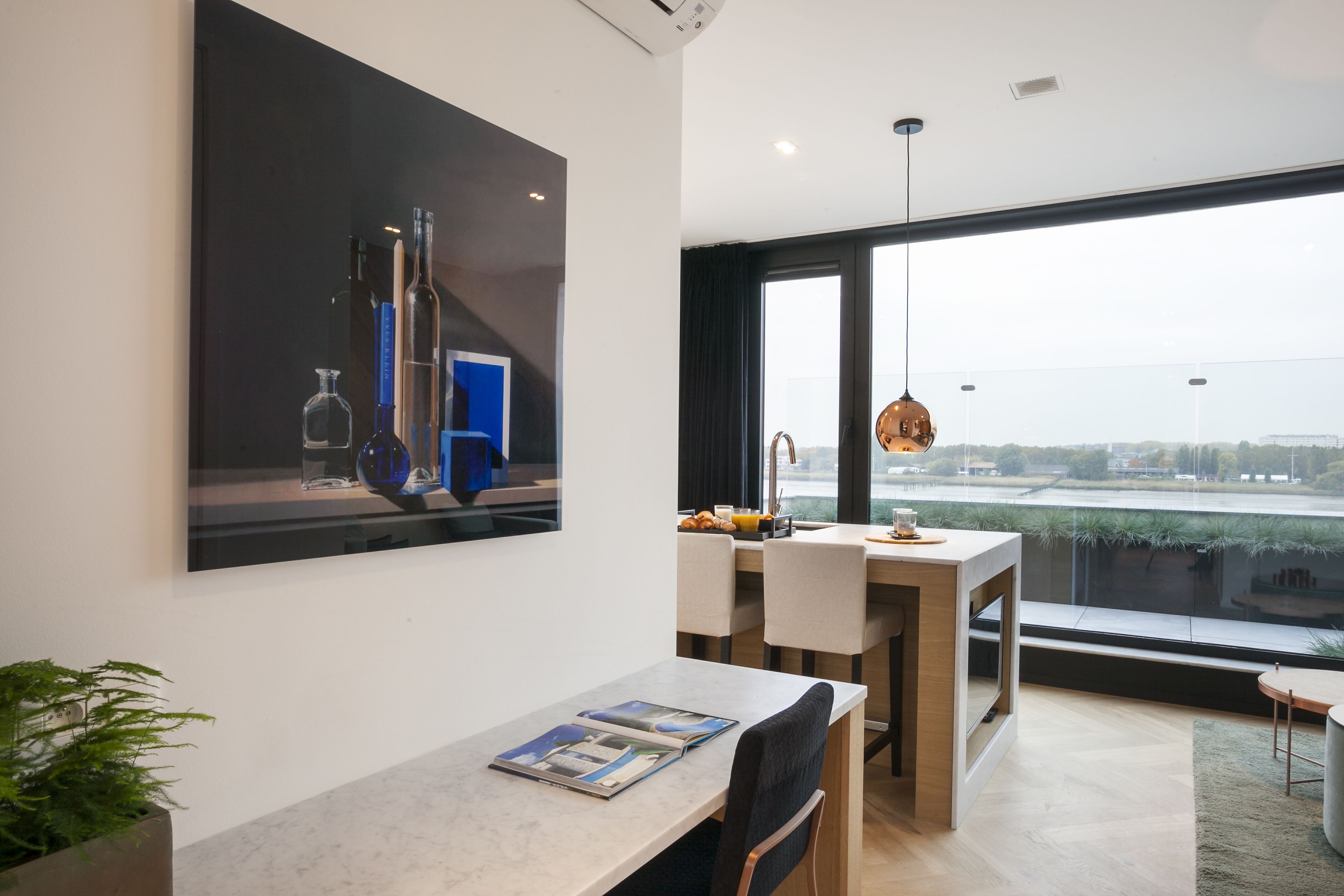 Een moderne eethoek met een groot raam, een tafel met tijdschriften en een schilderij aan de muur.