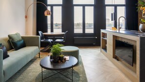 A modern living room with a sofa, a coffee table with plants, a dining area, and a kitchen with a TV. - Kaai 11 (Antwerp)
