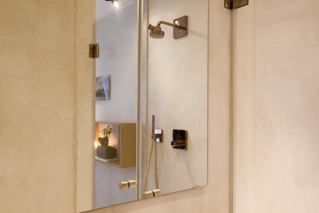 Een badkamer met een grote spiegel, een douche met een handdouche en een klein bedieningspaneel.