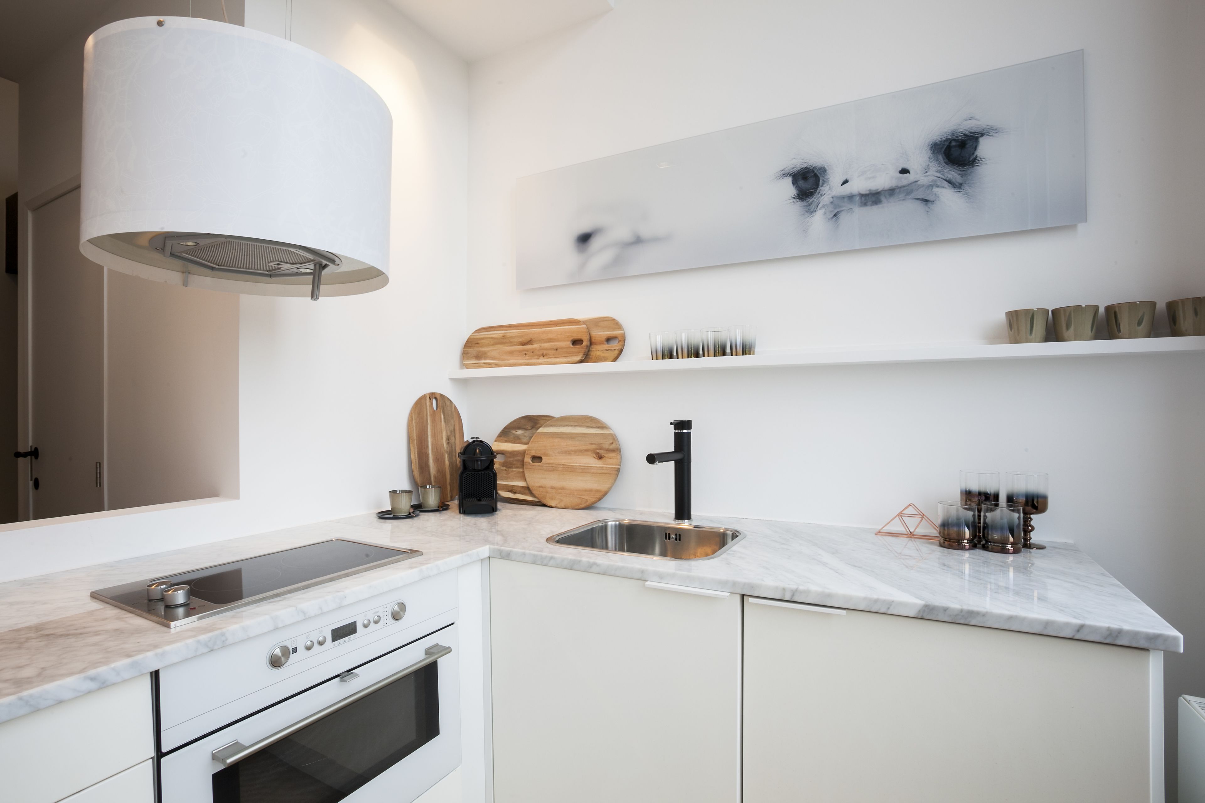 Une cuisine moderne dotée d’un four encastré, d’un évier en acier inoxydable et d’un plan de travail en marbre blanc.