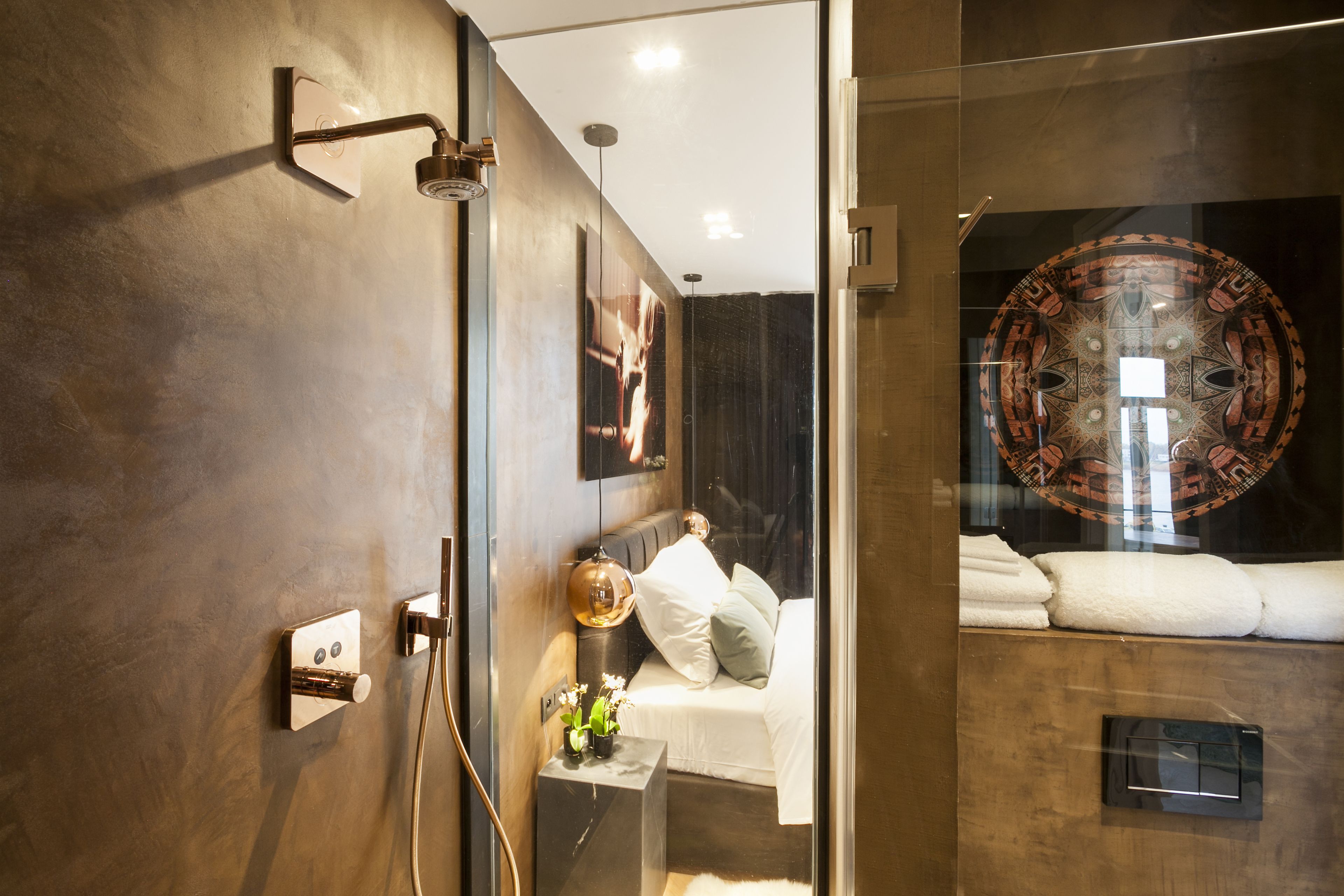 A modern bathroom with a glass shower enclosure, a bed with white linens, and a decorative wall piece.