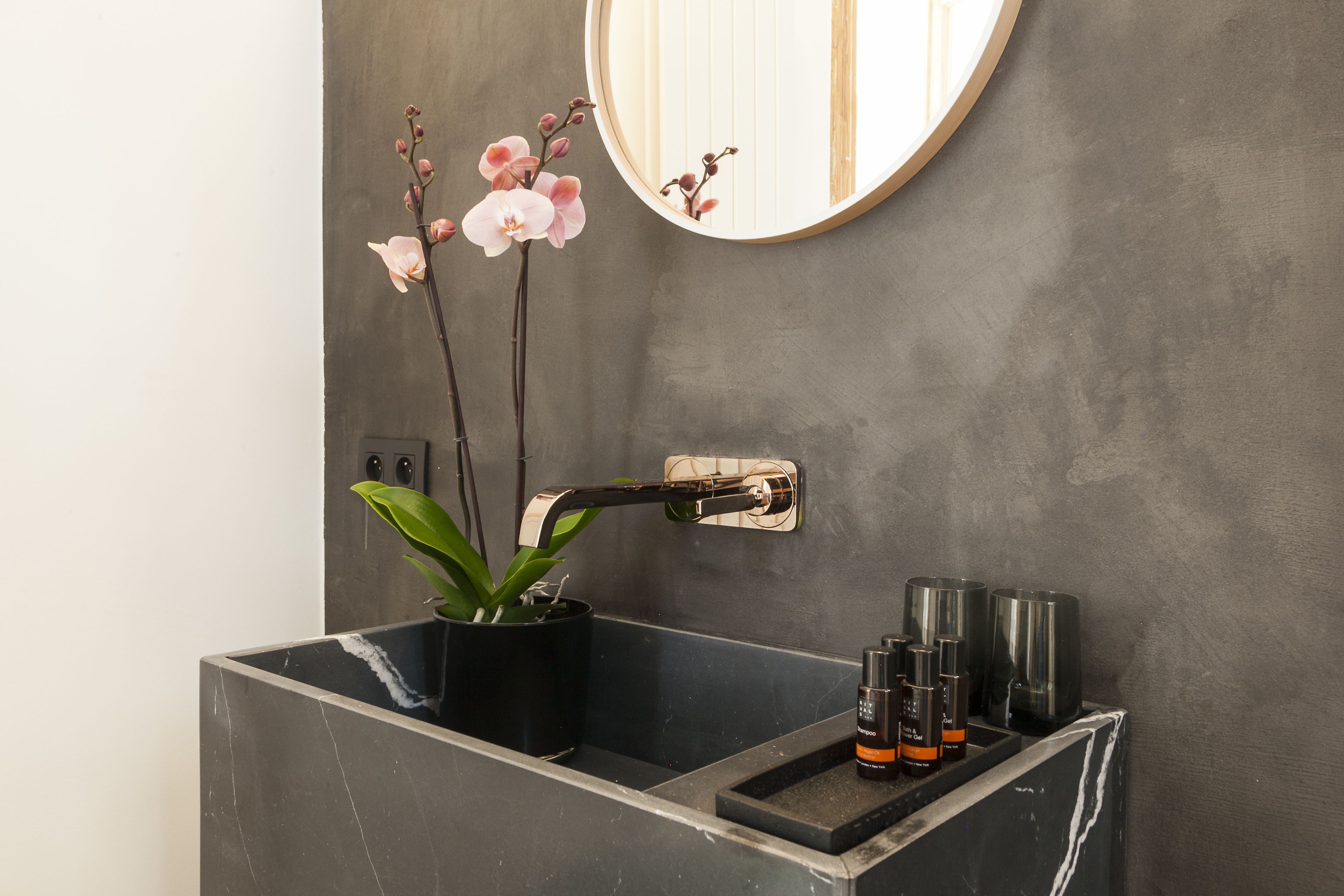 A bathroom with a marble sink, a mirror, and a potted orchid.
