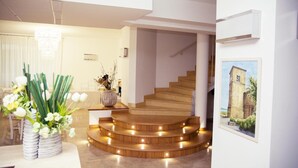 A modern interior with a wooden staircase, a chandelier, and a framed painting of a tower. - Hotel Di Nardo (Petacciato)