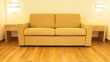 Een sofa in neutrale tinten, met twee bijzettafeltjes, een houten vloer en wandlampen.