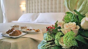 A hotel room with a bed, a breakfast table with croissants, and a floral arrangement. - Hotel Di Nardo (Petacciato)