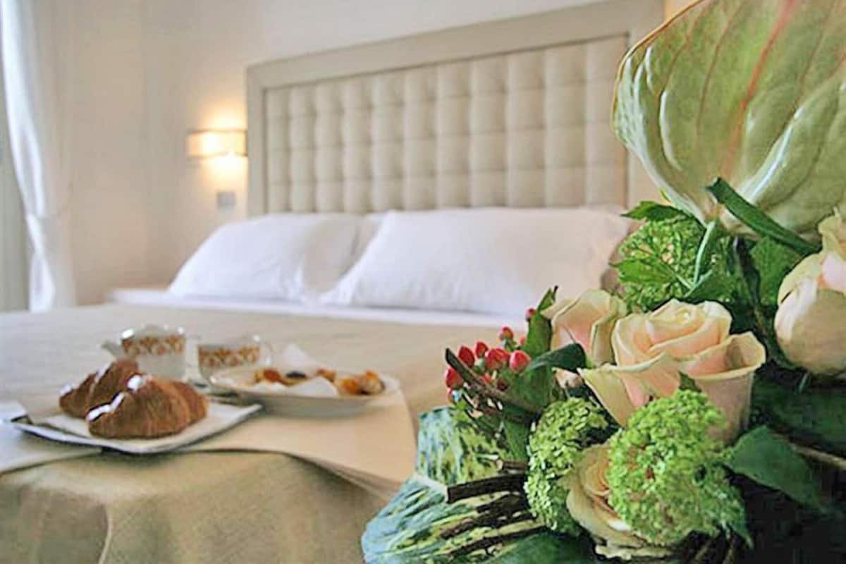 Una habitación de hotel con cama, una mesa de desayuno y croissants, además de un arreglo floral.