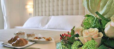 Una habitación de hotel con cama, una mesa de desayuno y croissants, además de un arreglo floral.