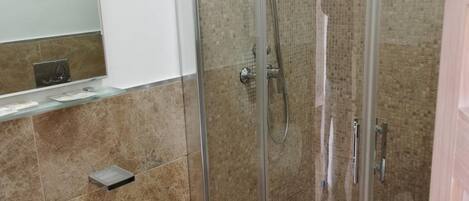Un baño moderno con ducha envuelta en cristal, lavamanos pedestal y espejo.