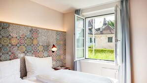 Une chambre à coucher avec un lit, une table de chevet, une lampe fixée au mur et une fenêtre avec des rideaux.